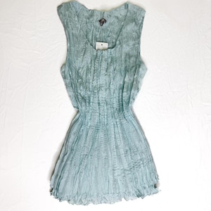 May include: A sleeveless, light blue top with a textured, crinkled fabric. The top has a square neckline and a gathered waist, with a ruffled hem. A small tag is attached near the neckline.