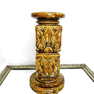 Puede incluir: Un portavelas decorativo de estilo vintage. El soporte de cerámica marrón presenta un diseño floral tallado detallado. La base y la parte superior son circulares, con una sección media cuadrada. El portavelas mide aproximadamente 25 cm de alto.