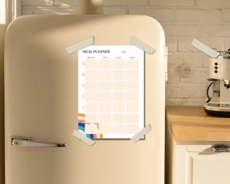 May include: A white meal planner with a colorful abstract design on the left side. The planner is labeled "Meal Planner" and has columns for breakfast, lunch, dinner, and snacks. The planner is attached to a beige refrigerator with tape.