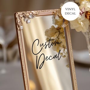 May include: Gold framed mirror with a custom vinyl decal that says "Custom Decal".