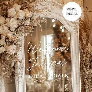 May include: A white framed mirror with the text "Welcome to Jessica's Bridal Shower March 19, 2024". The mirror is surrounded by floral arrangements of white roses and dried grasses. A "Vinyl Decal" sticker is in the upper right corner.