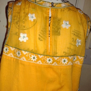 May include: A yellow sleeveless dress with white embroidered flowers and a green trim. The dress has a back zipper and is made of a sheer fabric.