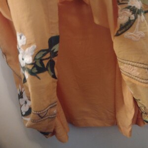 May include: A yellow maxi skirt with a floral print. The skirt has a white and green floral pattern with a brown trim.