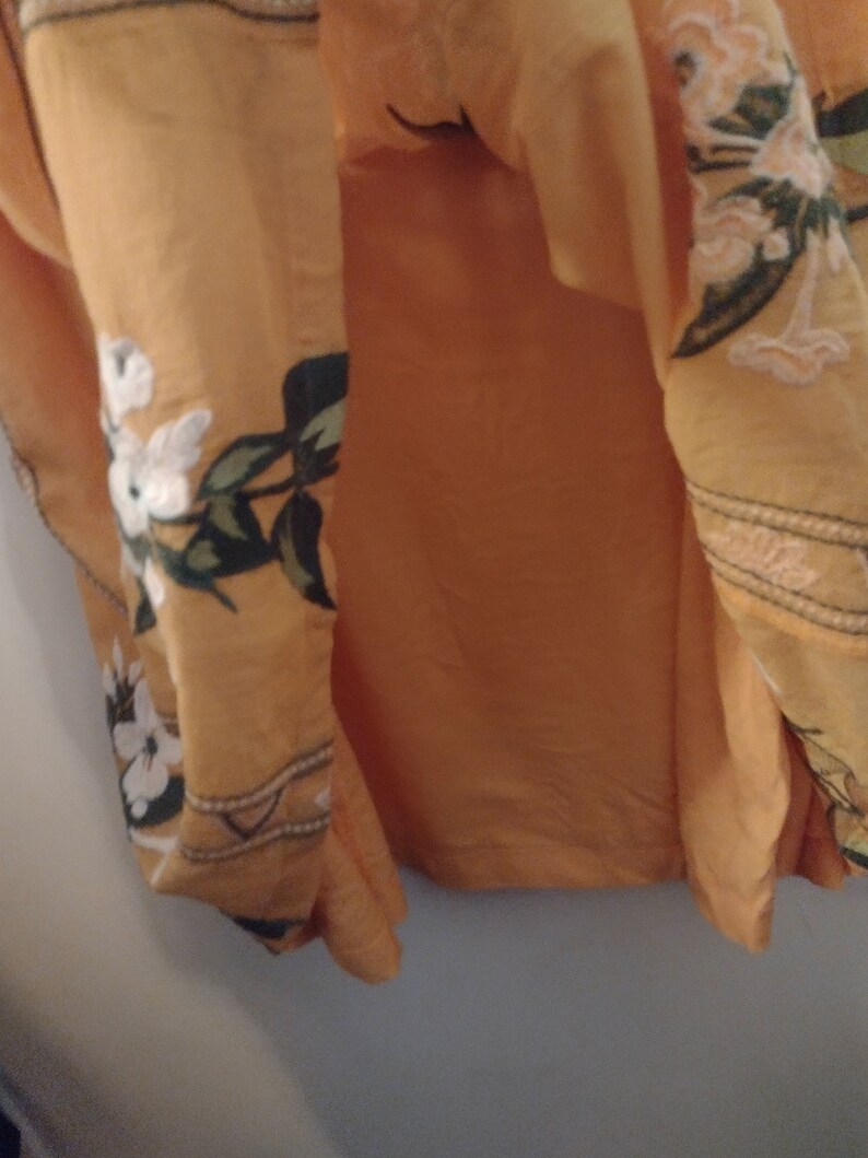May include: A yellow maxi skirt with a floral print. The skirt has a white and green floral pattern with a brown trim.