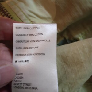 K&ouml;nnte beinhalten: Nahaufnahme eines Stoffetiketts mit Text in mehreren Sprachen, darunter "SHELL 100% COTTON" und "EXTERIOR 100% ALGODON." Das Etikett enth&auml;lt auch die Adresse "24 WEST STREET LONDON, WC2H9NA."