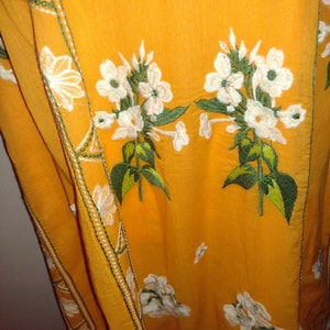 May include: A yellow fabric with white embroidered flowers and green leaves. The fabric has a white and green trim along the edge.