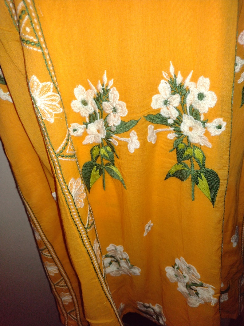 May include: A yellow fabric with white embroidered flowers and green leaves. The fabric has a white and green trim along the edge.