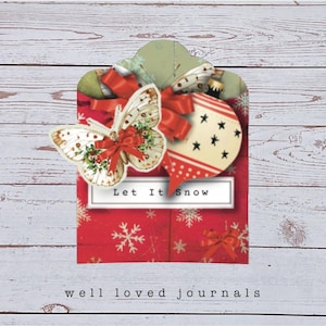 May include: A red and white Christmas-themed journal cover with a butterfly and ornament design. The cover features the text "Let It Snow" and is decorated with snowflakes and red bows. The words "well loved journals" are at the bottom.
