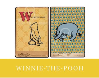 Puede incluir: Dos tarjetas de estilo vintage con el tema de Winnie the Pooh. Una presenta a Winnie the Pooh mirando hacia arriba a una gran "W" roja, la otra a Eeyore. Ambas tarjetas tienen un fondo amarillo con patrones florales y de estrellas.