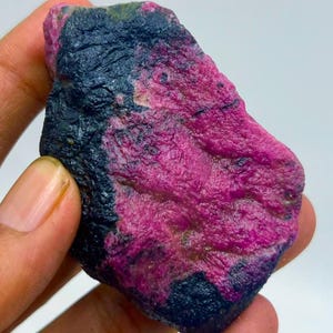 Peut inclure: Un spécimen minéral brut et non poli présentant un contraste saisissant entre des sections bleu marine profond et un centre magenta vif texturé. La pierre a une forme irrégulière et dentelée avec une texture de surface naturelle et rugueuse.