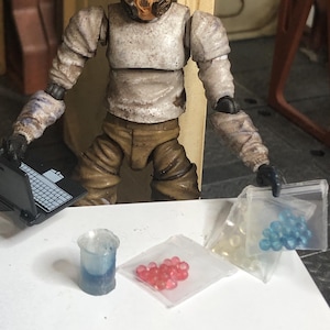 Puede incluir: Figura de acci&oacute;n detallada de una persona con traje y m&aacute;scara de protecci&oacute;n, sosteniendo una peque&ntilde;a computadora port&aacute;til. La figura est&aacute; rodeada de accesorios en miniatura.