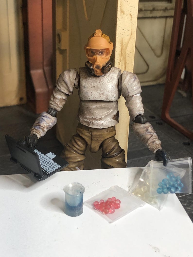 Puede incluir: Figura de acci&oacute;n detallada de una persona con traje y m&aacute;scara de protecci&oacute;n, sosteniendo una peque&ntilde;a computadora port&aacute;til. La figura est&aacute; rodeada de accesorios en miniatura.