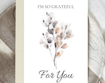 May include: A white greeting card with the text "I'M SO GRATEFUL For You" and a watercolor floral design in shades of gray, brown, and beige. The card is inside a light beige envelope.