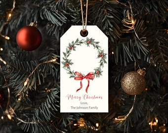 May include: A Christmas gift tag with a watercolor wreath design. The tag features a green wreath with red berries and a red bow. The text "Merry Christmas, Love, The Johnson Family" is printed in red script.