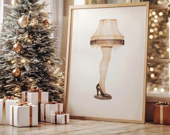 May include: A framed print of a leg lamp, a novelty item, with a beige lampshade and a leg in a fishnet stocking and high heel. The print is in a wooden frame, and is displayed near a decorated Christmas tree and wrapped gifts.