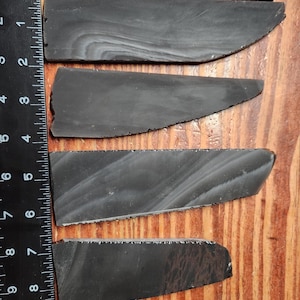 May include: Four flat, wedge-shaped pieces of dark gray stone with subtle lighter gray swirling patterns. The pieces are arranged vertically next to a black metal L-shaped ruler, which shows the longest piece is approximately 7.5 inches long.