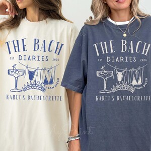 May include: Two oversized t-shirts, one cream and one denim, display a blue graphic. The design includes the text "THE BACH DIARIES 2026", a cocktail, swimwear, a crown, and "KARLI'S BACHELORETTE SAN DIEGO".