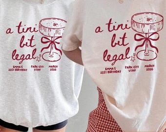 May include: Ash gray sweatshirt and ivory t-shirt with the text "a tini bit legal" in dark red. The design includes a cocktail glass illustration and event details: Emma's 21st birthday, Park City, Utah, March 2026.