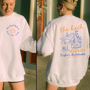 May include: White sweatshirt with blue and orange text and graphics. The text reads "the bach diaries Taylor's Bachelorette Miami, Florida 2023".