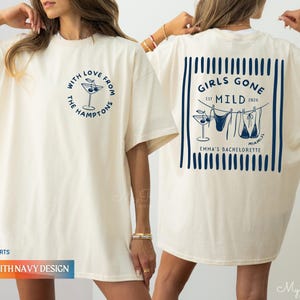 Puede incluir: Camiseta de color marfil con gr&aacute;ficos en azul marino. La parte delantera presenta un dise&ntilde;o de copa de c&oacute;ctel con el texto "With Love From The Hamptons". La parte trasera muestra "Girls Gone Mild" con gr&aacute;ficos de bikini y el texto "Emma's Bachelorette".