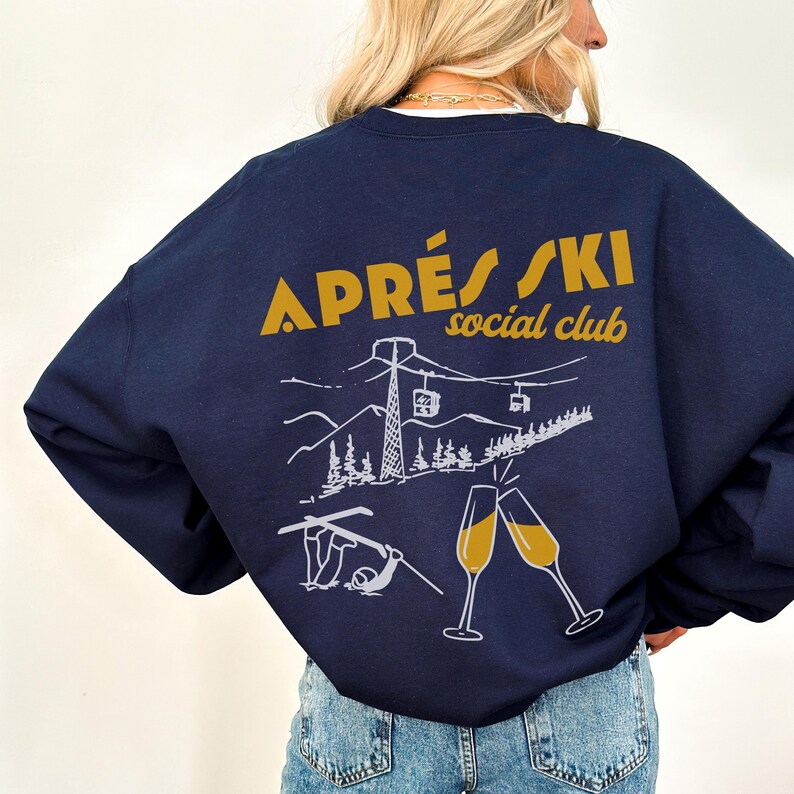 May include: A navy blue sweatshirt with a white graphic of a ski scene and the text "APR&Eacute;S SKI social club" in gold lettering.