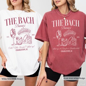 May include: Two white t-shirts with a pink design. The design features the text "The Bach Diaries" with a crown, a cocktail glass, and a cassette tape. One shirt says "Me? The Bride? Shut up! Charleston, SC" and the other says "Shut up, it's Taylor's Bachelorette! Charleston, SC".