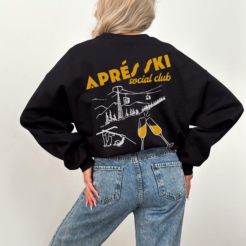 May include: Black sweatshirt with a white graphic of a ski lift, mountains, and champagne glasses. The text "APR&Egrave;S SKI social club" is printed in yellow on the back of the sweatshirt.