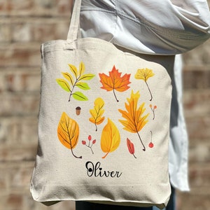 Może przedstawiać: Biała torba tote z płótna z wzorem kolorowych jesiennych liści i nadrukiem imienia "Oliver" z przodu.