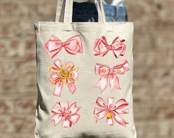 Puede incluir: Una bolsa de tela beige con un diseño de lazos rosas en la parte delantera. Los lazos son de varios estilos y tamaños, algunos con detalles dorados.