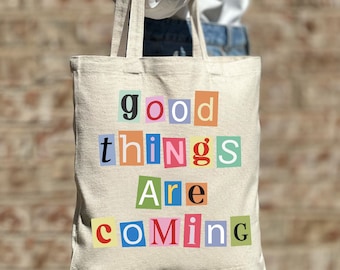 May include: A white canvas tote bag with the phrase "good things are coming" printed in colourful, cut-out letters.