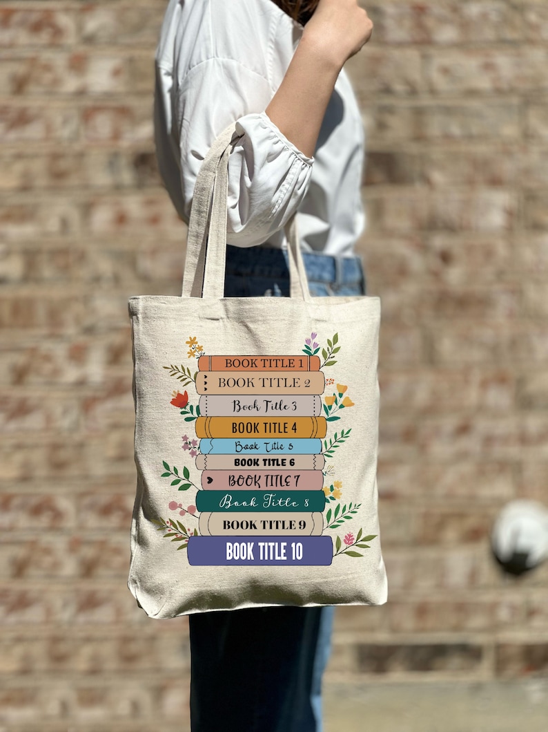 A woman holding a tote bag with a stack of ten books pictured on the bag