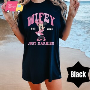 May include: Black t-shirt with a pink and white graphic of Mickey Mouse and the text "Wifey Est. 2024 Just Married".