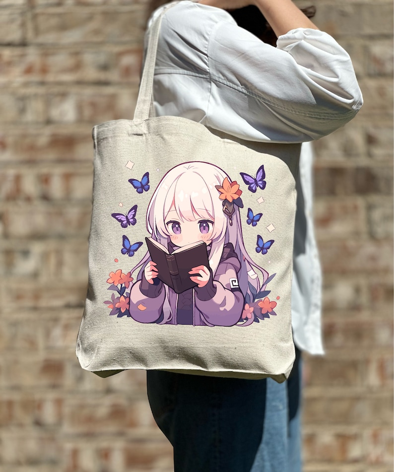 May include: A white canvas tote bag featuring a design of a young girl with long white hair reading a book. The girl is surrounded by purple flowers and blue butterflies.