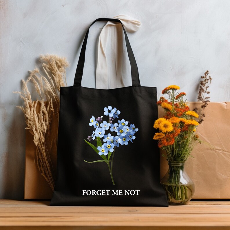 May include: Black tote bag with a white strap and a floral design of blue forget-me-not flowers. The bag has the text "Forget Me Not" printed on the bottom.