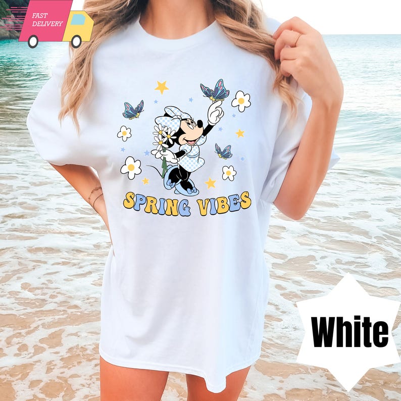 Pode incluir: Camiseta branca com uma imagem de desenho animado da Minnie Mouse segurando uma flor e borboletas. O texto "Spring Vibes" &eacute; impresso abaixo da imagem.