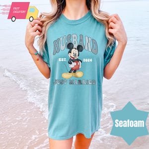 May include: A light blue t-shirt with a graphic of Mickey Mouse and the text "Husband Est. 2024 Just Married".