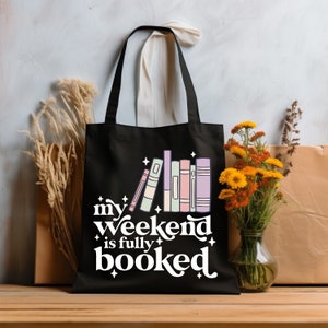 May include: Black tote bag with a white graphic that says "my weekend is fully booked" and a stack of colorful books.