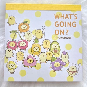 May include: A yellow notepad with a yellow border and a white background. The notepad has a polka dot pattern and features a cartoon illustration of various fruits and birds. The text "WHAT'S GOING ON? PIYOKOMAME" is printed on the notepad.