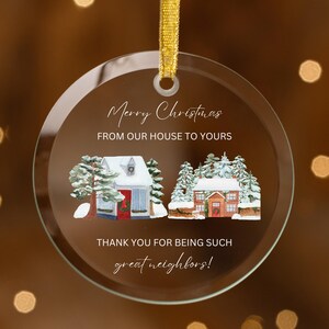 Könnte beinhalten: Ein runder Weihnachtsbaumschmuck aus Glas mit weißem Hintergrund und der Aufschrift "Frohe Weihnachten von unserem Haus zu Ihrem. Vielen Dank, dass Sie so gute Nachbarn sind!" Der Schmuck zeigt zwei Illustrationen von schneebedeckten Häusern mit roten Türen und schneebedeckten Bäumen.