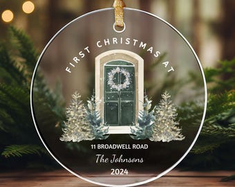 May include: A round glass ornament with a watercolor illustration of a front door with a wreath, two small pine trees, and the text "First Christmas at 11 Broadwell Road The Johnsons 2024".