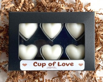 May include: A black box with a clear window showing six white heart-shaped wax melts. The box has the text "Cup of Love" on the front.