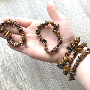 May include: Three tiger eye chip bead bracelets. The bracelets are made of small, irregularly shaped, polished brown and gold stones strung together on elastic. The bracelets are displayed on a person's hand and wrist.