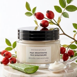 May include: A jar of Skin Food Naturelle Kojic Brightening Face Moisturizer, 2 oz, with a black lid, sits on a marble surface. The jar is next to a sprig of red berries and a piece of aloe vera. A spoonful of moisturizer is also visible.