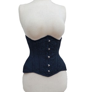 Könnte beinhalten: Ein marineblauer Korsett mit floralem Muster wird auf einer Schaufensterpuppe gezeigt. Das Korsett hat einen geschwungenen Ausschnitt und wird mit silberfarbenen Verschlüssen geschlossen. Der Stoff hat einen dezenten Glanz.