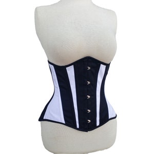 Könnte beinhalten: Ein marineblau-weiß gestreifter Korsett auf einer Schaufensterpuppe. Das Korsett hat vertikale Streifen, silberfarbene Ösen und eine geschwungene Silhouette. Das Kleidungsstück ist aus Stoff.