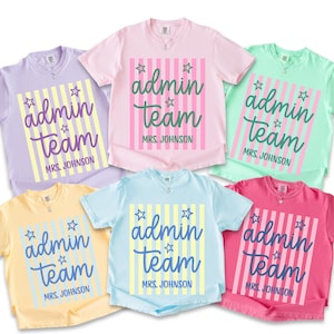 May include: Six short-sleeve crew neck t-shirts in lavender, light pink, mint green, pale yellow, light blue, and hot pink. Each shirt features a central rectangular graphic with vertical stripes, the text "admin team", and "MRS. JOHNSON".
