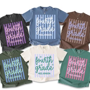May include: Six short-sleeve crew neck t-shirts in black, blue, brown, olive green, cream, and teal. Each shirt features a central graphic with vertical stripes, the text "fourth grade" in script, small star icons, and "MISS JOHNSON" below.