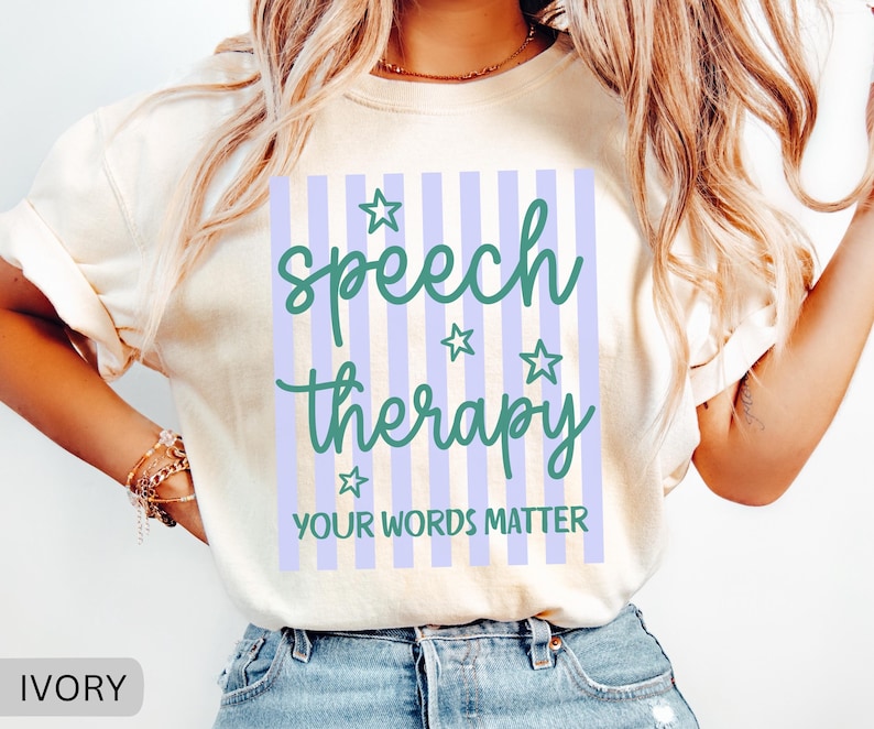 May include: An ivory short-sleeve t-shirt featuring a graphic design with vertical light purple stripes. The text reads "speech therapy" in a dark green script font, accompanied by four small stars and the text "YOUR WORDS MATTER" below.