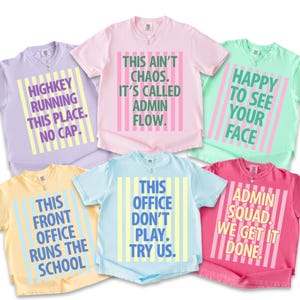May include: A collection of six short-sleeved t-shirts in various pastel colors, each with a unique text-based design. The shirts feature phrases like "Highkey Running This Place. No Cap" and "Admin Squad. We Get It Done."