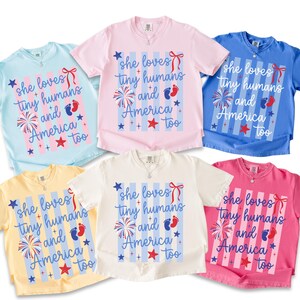 May include: Six short-sleeve t-shirts in light blue, light pink, blue, yellow, white, and dark pink. Each shirt features a graphic with vertical stripes, a red bow, a firework, baby footprints, and the text: she loves tiny humans and America too.